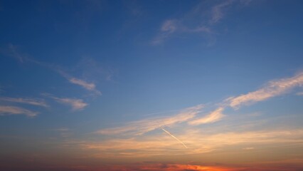 A serene sunrise with a sky that transitions from deep blue at the top to warm orange hues near the horizon. Wispy clouds are gently scattered, adding to the tranquil ambiance. 
