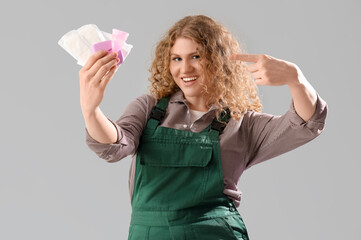 Female worker pointing at feminine hygiene items on grey background