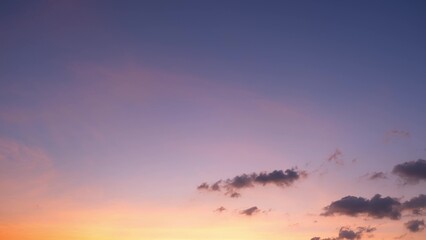 A beautiful sunset with a sky transitioning from warm orange and yellow tones near the horizon to soft pink and purple hues higher up. Dark, scattered clouds add contrast to the serene scene.
