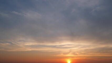 A serene sunrise with the sun just above the horizon, casting a warm orange glow across the sky. Soft clouds scatter the light, creating a gradient of colors from orange to blue. Cloud background.
