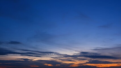 Obraz premium A tranquil sunrise with a deep blue sky gradually lightening towards the horizon. Dark clouds add depth to the scene, while a hint of orange at the bottom signifies the rising sun. Cloud background. 