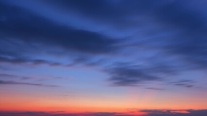 A stunning sunrise with deep blue clouds spread across the sky, gradually transitioning to a warm orange and pink hue near the horizon, creating a beautiful gradient. Sunrise sky background.
