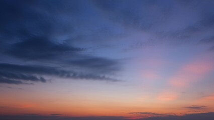 A serene sunrise with a deep blue sky transitioning to soft pink and orange hues near the horizon, accentuated by wisps of dark clouds creating a tranquil, early morning scene. Cloud background.
