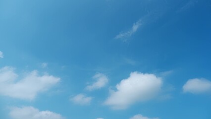 A bright blue sky scattered with fluffy white clouds. The serene, clear sky and soft clouds create...