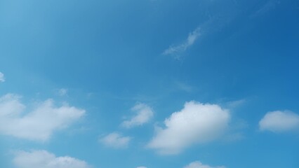 A bright blue sky scattered with fluffy white clouds. The serene, clear sky and soft clouds create a peaceful and calming atmosphere, indicative of a beautiful day. Wonder of nature background.
