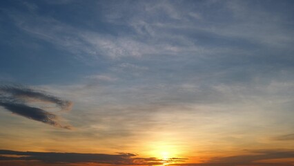 Naklejka premium A stunning sunrise with a mix of golden and orange hues at the horizon, gradually blending into the blue sky above. Wispy clouds are scattered, adding texture to the serene scene. Cloud background. 