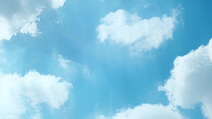 A serene blue sky scattered with fluffy white clouds. The clouds have a soft, wispy appearance,...
