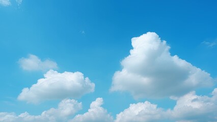 A clear blue sky with a few large, fluffy white clouds floating gently. The clouds are well-defined against the vivid blue background, creating a bright and peaceful scene. Nature background.
