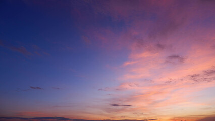 A serene sunrise with a sky transitioning from deep blues at the top to warm pinks and oranges near the horizon. Wispy clouds are gently illuminated by the rising sun. Sunrise sky background.
