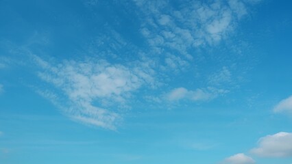 A bright blue sky with scattered white, fluffy clouds. The clouds are sparse, allowing the vibrant blue of the sky to dominate the scene, creating a serene and peaceful atmosphere. Cloud background.
