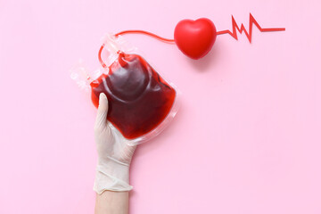 Female hand in rubber glove with blood pack, heart and cardiogram on pink background. World Blood...