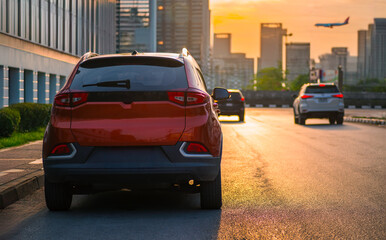 Urban traffic scene during sunset with cars on the road and an airplane flying over a modern...