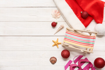 Christmas balls, Santa's hat, tiny deck chair and kid's flip-flops on white wooden background. Top...