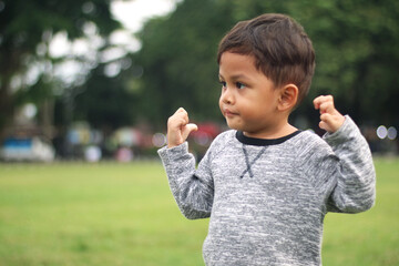 A handsome young boy, nicely dressed showing an expression of joy with hands up in the air looking excited and happy to be playing outdoors.
