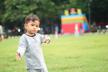 A handsome young boy, nicely dressed showing an expression of joy with hands up in the air looking excited and happy to be playing outdoors.
