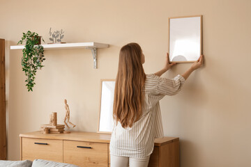 Young woman hanging blank frames on beige wall in modern living room