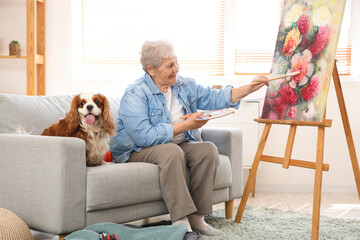 Senior woman with cute cavalier King Charles spaniel dog painting at home