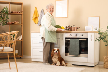 Senior woman with vegetables and cute cavalier King Charles spaniel dog in kitchen