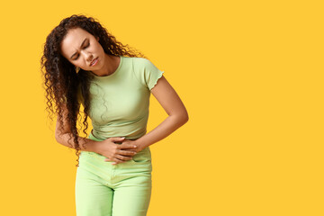 Young African-American woman with stomach ache on yellow background