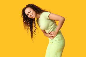 Young African-American woman with stomach ache on yellow background
