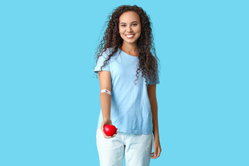 Young female African-American blood donor with applied medical patch and heart on blue background