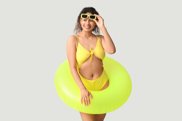 Beautiful young African-American woman in stylish yellow swimsuit with inflatable ring on grey...