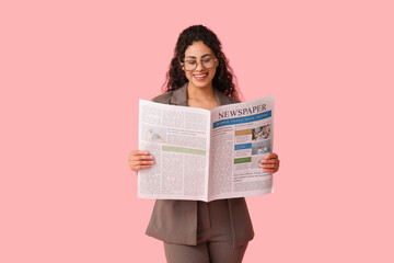 Beautiful young African-American woman reading newspaper on pink background