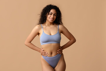 Beautiful young happy African-American woman in stylish underwear on beige background