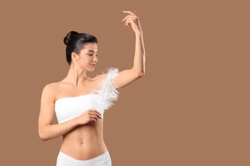 Beautiful young happy woman with soft feather on brown background. Depilation concept