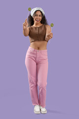 Beautiful young happy African-American woman holding sticks with kiwi on purple background