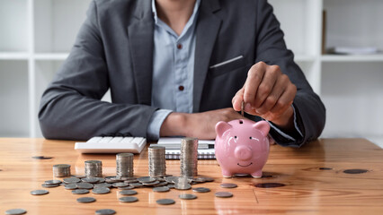 Businessman saving money with piggy bank and coins on desk, financial planning and investment...