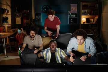 Group of ethnically diverse young men spending evening at home watching football game match on TV, copy space © AnnaStills