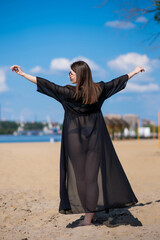 Beautiful, attractive, happy girl posing on a sandy beach on a sunny day in a blue swimsuit, sunglasses and a black beach tunic. Beachwear