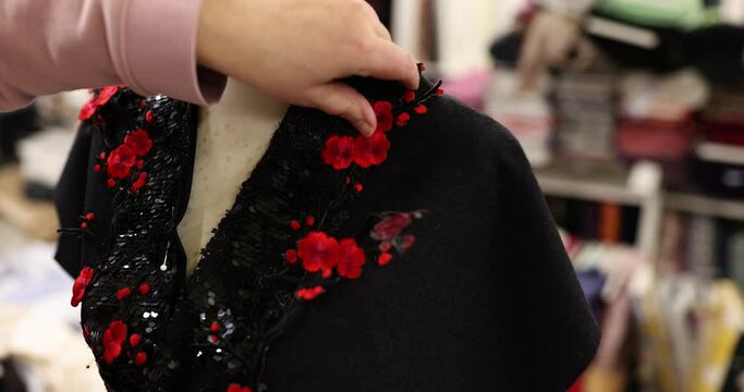 Closeup of dressmaker hands sewing red flower shaped sequins onto black sequined dress