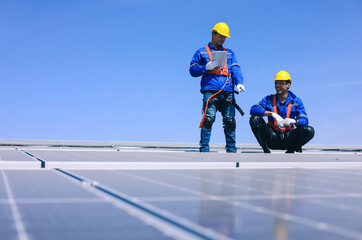 Two young engineers using tablet to inspect solar panels on the roof of industrial factory for...