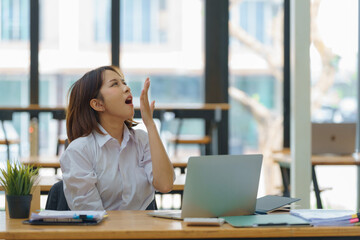 Asian businesswoman yawning while working with a laptop computer.