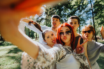 A group of diverse young friends enjoying their day in the park, playfully taking a selfie with...