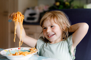 Adorable toddler girl eat pasta spaghetti with tomato bolognese with minced meat. Happy preschool...