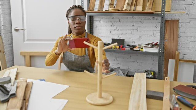 African american woman with braids photographing a wooden model in a carpentry workshop