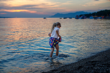 Little girl walking on beautiful ocean beach. Happy preschool child play by sunset on sea beach. Family vacations with children in summer.