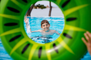 Cool school boy having fun on inflatable rubber circle in outdoor pool. Summer holiday. Summertime...