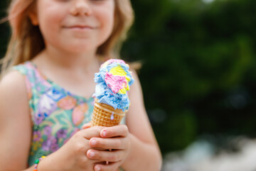 Happy preschool girl eating colorful ice cream in waffle cone on sunny summer day. Little toddler child eat icecream dessert. Sweet food on hot warm summertime days. Bright light, colorful ice-cream
