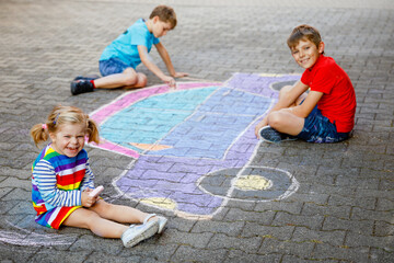 three little children, two school kids boys and toddler girl having fun with with car picture drawing with colorful chalks on asphalt. Siblings painting on ground playing together. Creative leisure