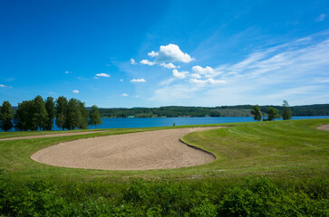 Golf course green grass and sand bunker next to a lake and forest on the horizon on a sunny day...