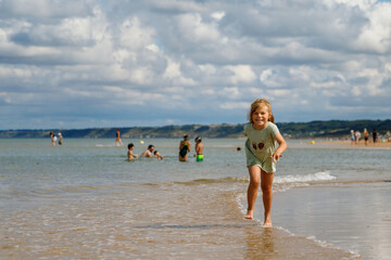 Fototapeta premium Happy preschool girl having fun on the sand beach Omaha at Atlantic coast of Normandy, France. Outdoor summer activities for kids