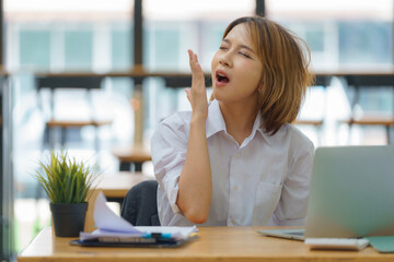 Asian businesswoman yawning while working with a laptop computer.