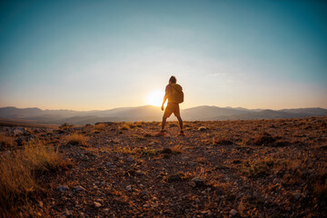 hiking in the mountains. a man with a backpack stands on a mountain against the backdrop of sunset....