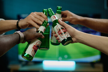 Closeup shot of hands of unrecognizable men clinking bottles with beer while watching soccer game...