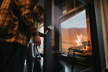 A young man is seen feeding wood into a roaring fireplace, creating a warm and inviting atmosphere...