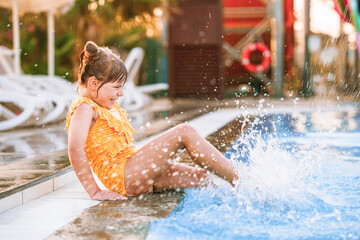 Little preschool girl playing in outdoor swimming pool by sunset. Child learning to swim in outdoor...